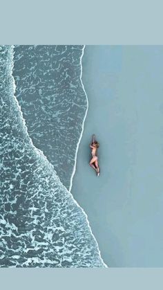 an aerial view of a woman laying on her stomach in the water at the beach