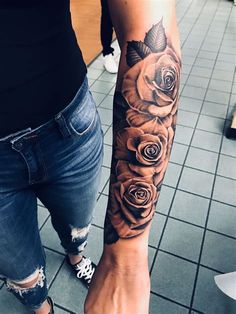 a woman with a rose tattoo on her arm and hand is standing in front of a tiled floor