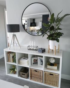 a white shelf with baskets and plants on it in front of a round mirror above the bookshelf