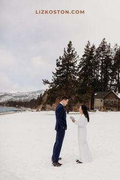 a bride and groom standing in the snow holding each other's hand while looking at each other