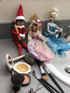 two dolls sitting on top of a sink next to makeup