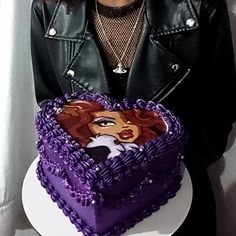 a woman holding a heart shaped cake in front of her face and wearing a leather jacket