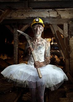 a man in a white tutu holding a large wooden stick and wearing a yellow hard hat