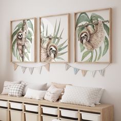 three sloths hanging on the wall above a bench with pillows and baskets underneath them