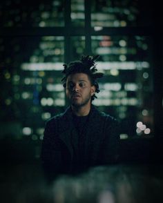 a man with dreadlocks standing in front of a cityscape at night