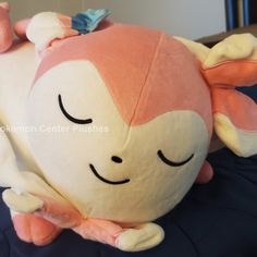 a pink and white stuffed animal laying on top of a blue bed sheet with its eyes closed