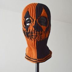 an orange and black knitted skull mask on a stick with the word, halloween written on it