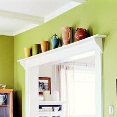 a living room with green walls and white trim on the wall, decorated with vases