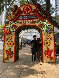 two people standing in front of a colorful archway with flowers and butterflies painted on it