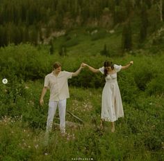 a man and woman holding hands while standing in a field with wildflowers behind them