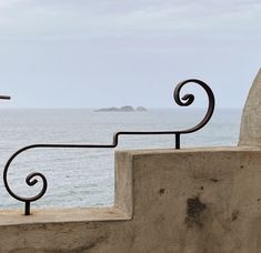 an iron railing next to the ocean with a cross in the distance and a rock outcropping