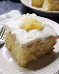 a piece of cake with white frosting and pineapple on top sits on a plate next to a fork