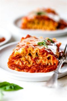 two white plates topped with lasagna sauce and green garnish on the side