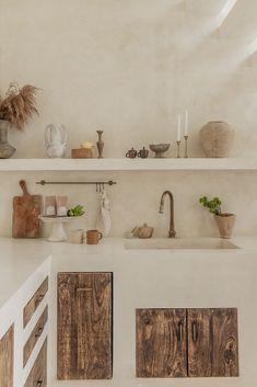 a white kitchen with wooden cabinets and shelves filled with pots, vases and other items