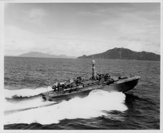 a black and white photo of a boat in the water with mountains in the background