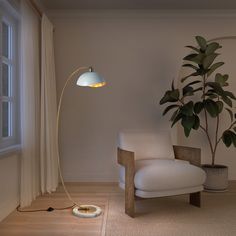 a white chair sitting next to a lamp on top of a wooden floor near a potted plant