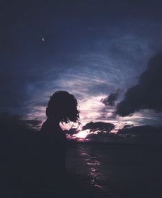 the silhouette of a person standing in front of a body of water at night time