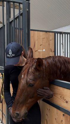 a woman is petting a horse in an enclosed area with wooden walls and metal railings