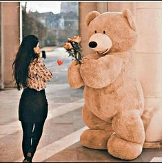 a woman standing next to a giant teddy bear with flowers in it's mouth