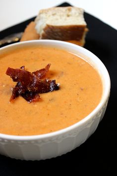 a white bowl filled with soup next to a slice of bread on a black plate