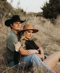 a man and woman sitting on the ground in tall grass with trees in the background