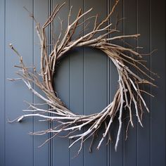 a twig wreath hanging on the side of a door with blue siding and wood paneling