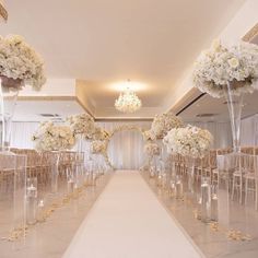 the aisle is lined with clear chairs and white flowers