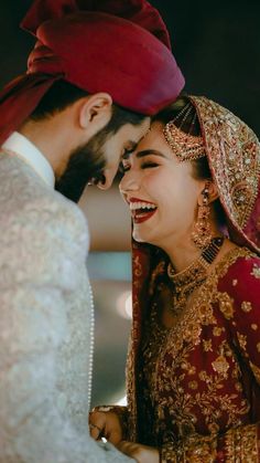 a bride and groom laughing together in their wedding outfits, with one wearing a red turban