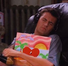 a man sitting in a chair with a book on his lap and headphones to his ears