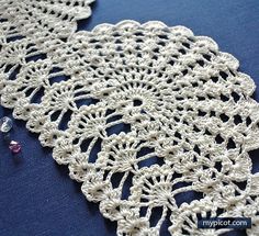 two crocheted doily are laying on a blue tablecloth with pins in it