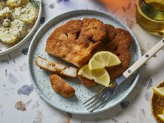 a white plate topped with fried fish next to lemon wedges and mashed potatoes