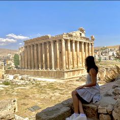 a woman sitting on top of a rock next to an ancient building