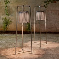 two metal lamps sitting next to each other on top of a cement floor near a wall