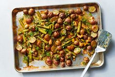 a pan filled with potatoes and asparagus on top of a white table next to a spatula