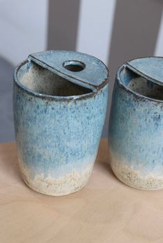 two blue and white pots sitting on top of a wooden table next to each other