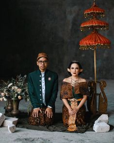 a man and woman sitting next to each other in front of a table with an umbrella