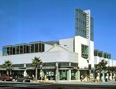 the building is white and has many people walking around in front of it, along with palm trees