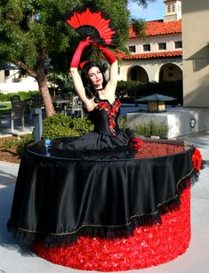 a woman in a black and red dress sitting on top of a table with a fan