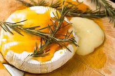 a piece of cheese is sitting on a cutting board with some rosemary sprigs