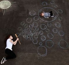 a woman sitting on the ground drawing bubbles with chalk and a baseball bat in front of her