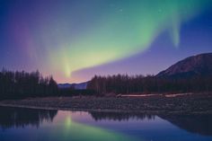 an aurora bore is reflected in the water at night with trees and mountains in the background