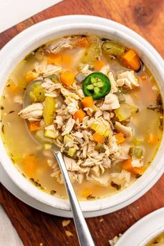 a white bowl filled with chicken and vegetable soup on top of a wooden cutting board