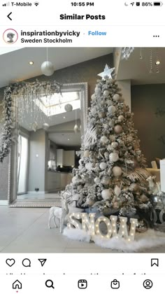 a white christmas tree with silver ornaments and snowflakes on it, in front of a mirror