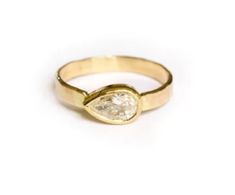 a yellow gold ring with a pear shaped diamond on the front and side, set against a white background