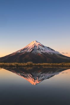 a mountain with snow on top is reflected in the still water at sunset or dawn