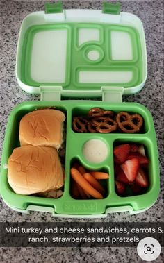 a green lunch box filled with sandwiches, pretzels and fruit on the side