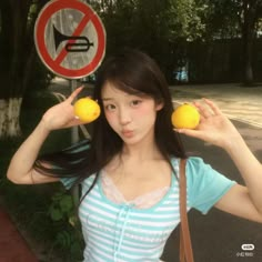 a young woman holding two lemons in front of her face while standing next to a street sign