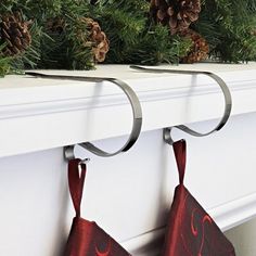 two christmas stockings hanging on a fireplace mantel with pine cones and evergreen branches in the background