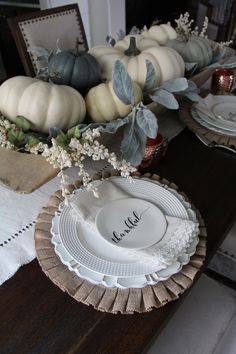 the table is set with white plates and pumpkins