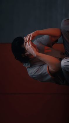 a man in grey and orange shirt holding his hands to his face while sitting on a red bench